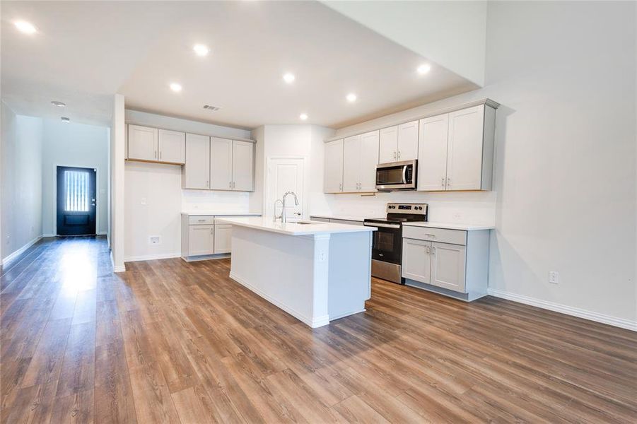 Kitchen featuring sink, appliances with stainless steel finishes, wood-type flooring, and a center island with sink