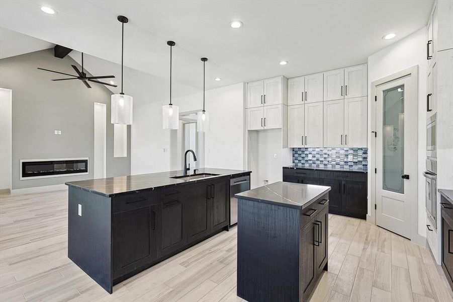 Kitchen featuring sink, ceiling fan, lofted ceiling, a center island with sink, and white cabinets