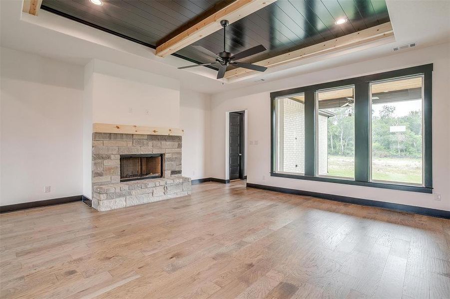 Unfurnished living room featuring ceiling fan, beamed ceiling, a fireplace, light wood-type flooring, and a raised ceiling