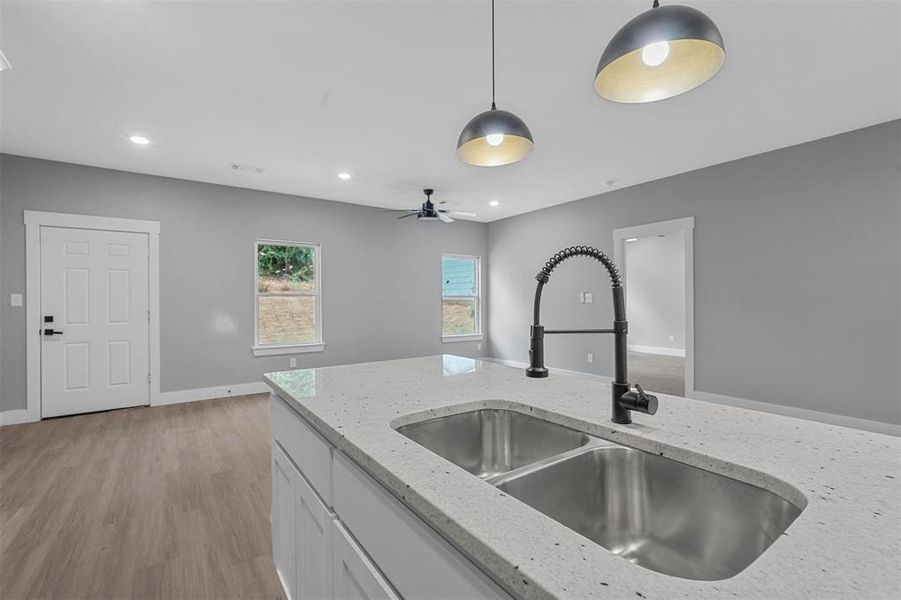 Kitchen featuring decorative light fixtures, sink, ceiling fan, light stone counters, and light wood-type flooring