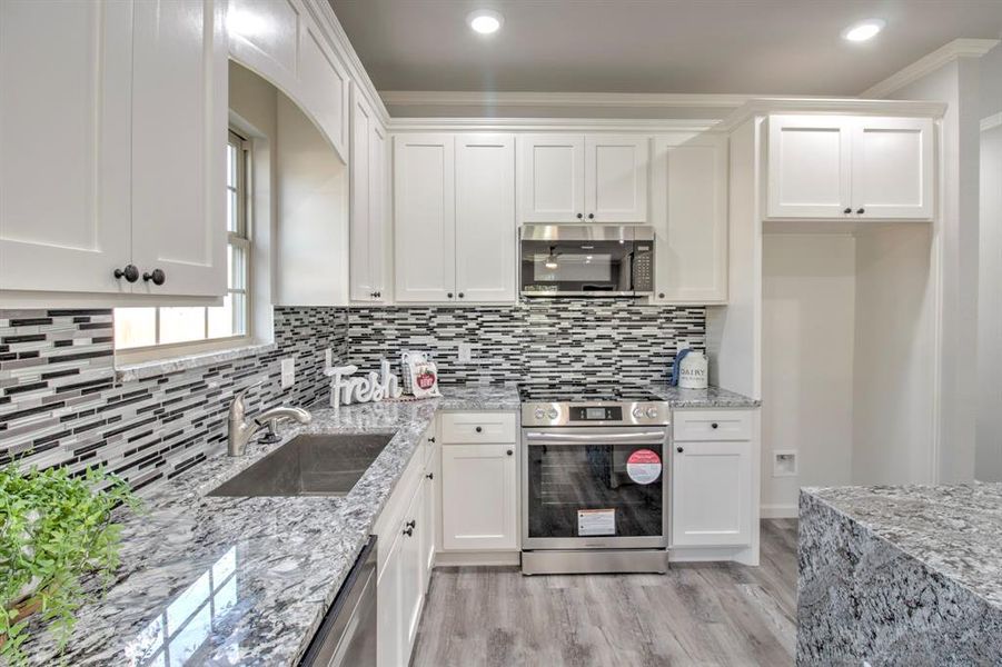 Kitchen featuring sink, appliances with stainless steel finishes, ornamental molding, light stone countertops, and white cabinets