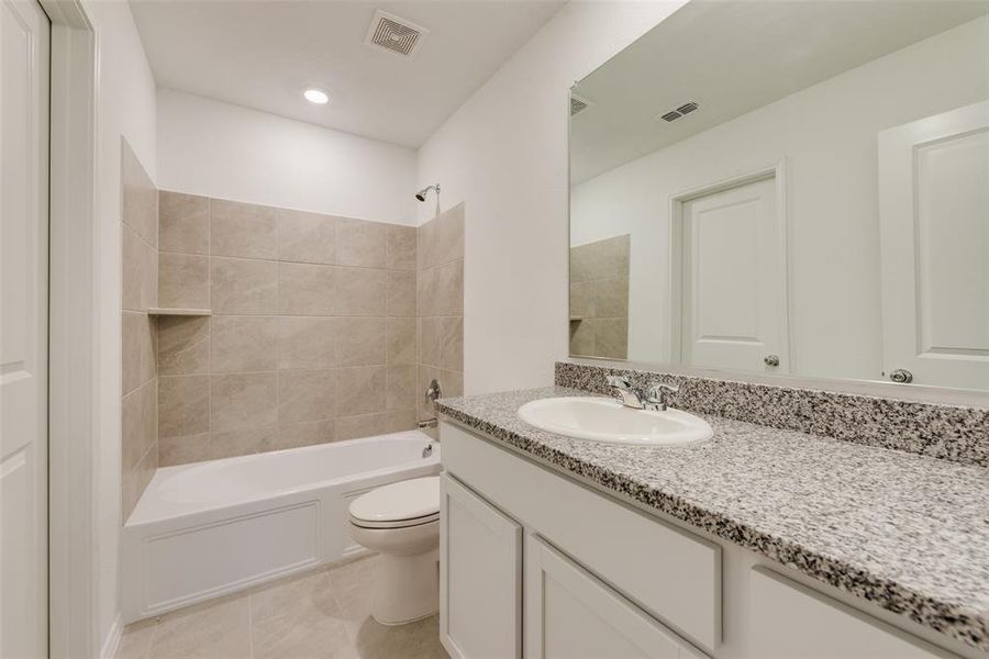 Full bathroom with vanity, tile patterned flooring, tiled shower / bath, and toilet