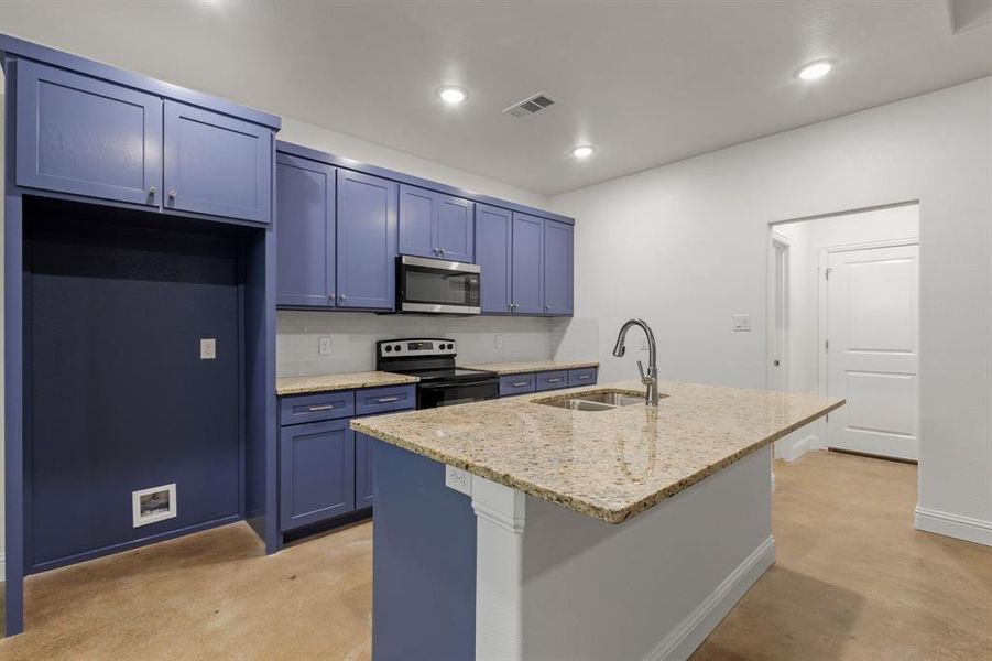 Kitchen with an island with sink, stainless steel appliances, sink, blue cabinetry, and light stone counters