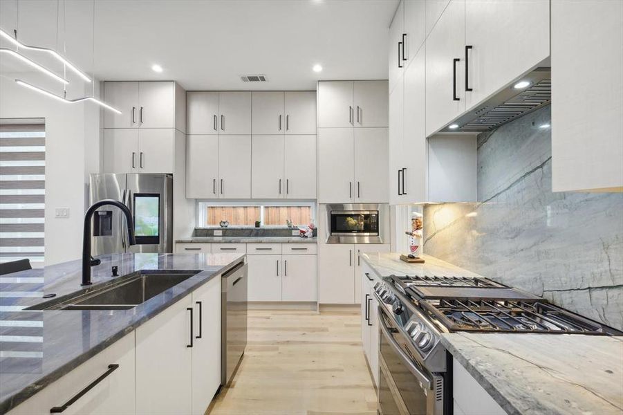 Kitchen featuring tasteful backsplash, dark stone countertops, appliances with stainless steel finishes, and light wood-type flooring