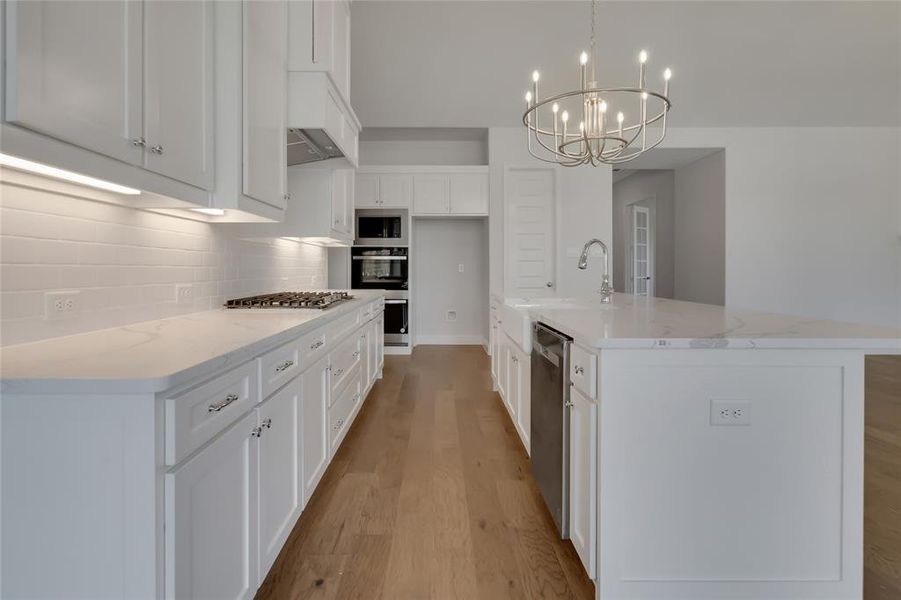 Kitchen with backsplash, light hardwood / wood-style floors, white cabinetry, a center island with sink, and hanging light fixtures