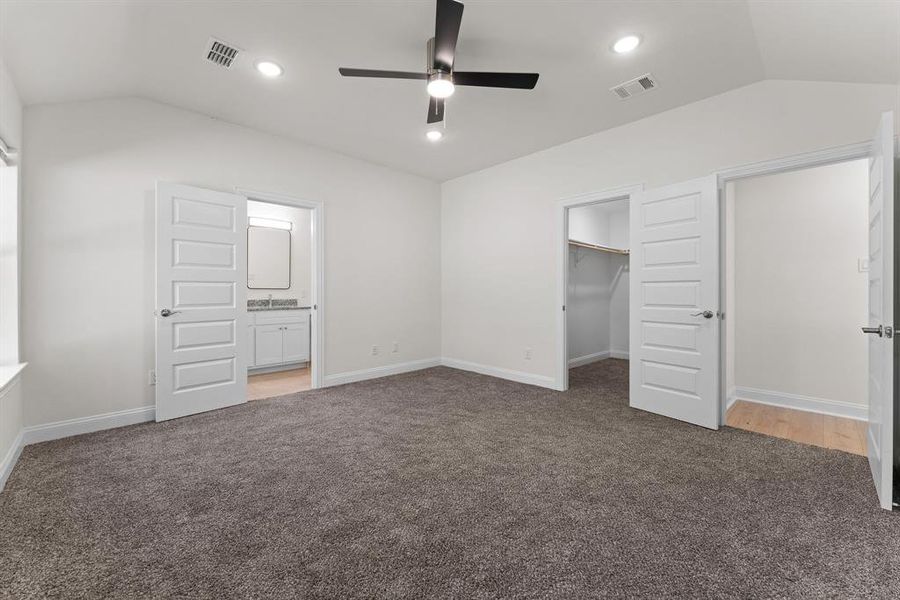 Owners bedroom with lofted ceiling, a closet, dark carpet, a walk in closet, and ceiling fan