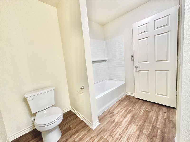 Bathroom featuring tub / shower combination, hardwood / wood-style flooring, and toilet