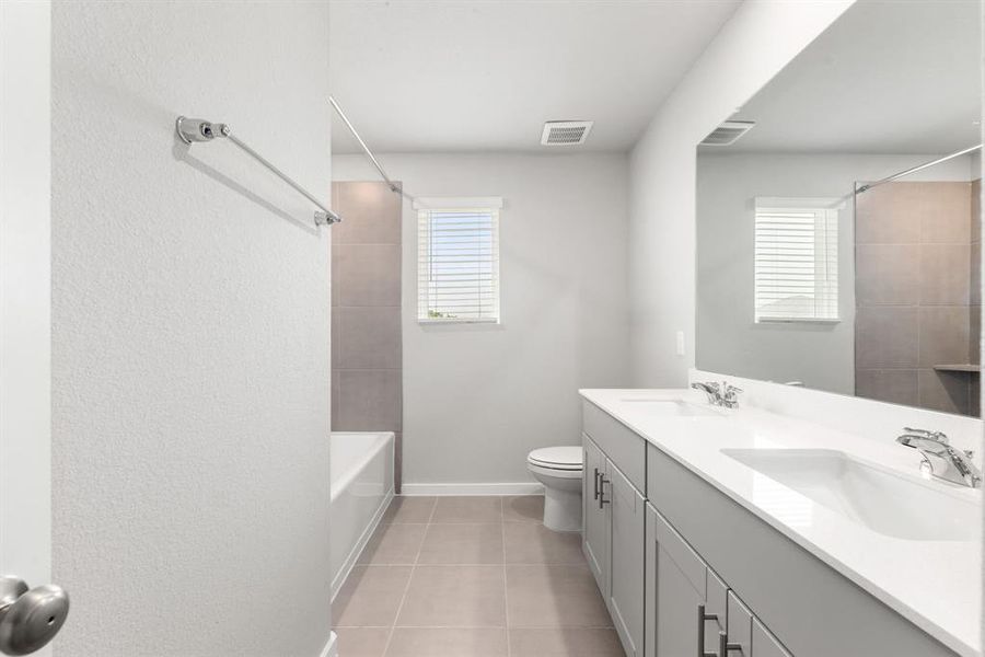 Secondary bathroom features double sinks, Quartz countertops, neutral paint, shower/tub combo with tile surround, large mirror, tile floors, sleek fixtures and modern finishes, plenty of space to accommodate any visiting family or guests.