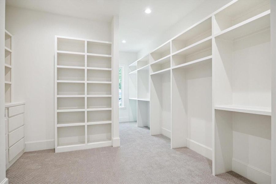 This is a bright, spacious walk-in closet featuring built-in white shelving units, perfect for organizing a large wardrobe and accessories. The carpeted floor adds a cozy touch.