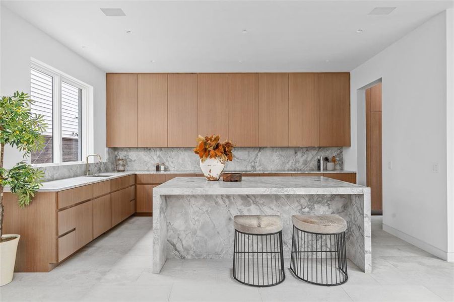 This stunning kitchen showcases sleek rift-cut walnut cabinets that offer a clean, modern aesthetic. The luxurious leathered quartzite countertops and matching backsplash provide both durability and elegance, creating a sophisticated space for cooking and entertaining. The spacious island adds functionality with plenty of space for enjoying a casual meal on the go.