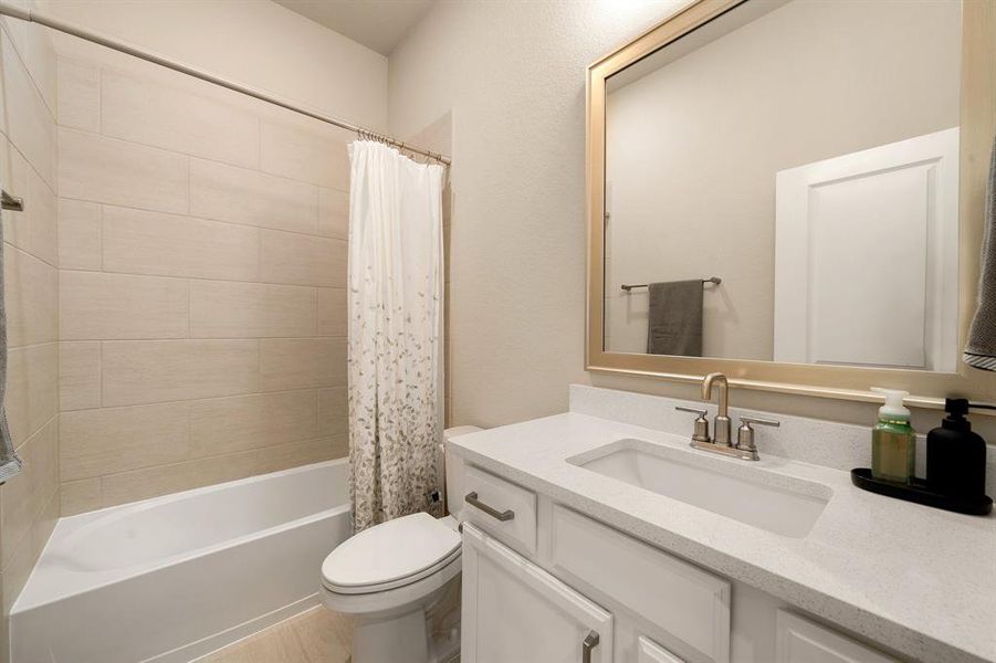 Secondary bathroom features Quartz countertops and cabinets, neutral paint, shower/tub combo with tile surround, large framed mirror, tile floors, sleek fixtures and modern finishes, plenty of space to accommodate any visiting family or guests.