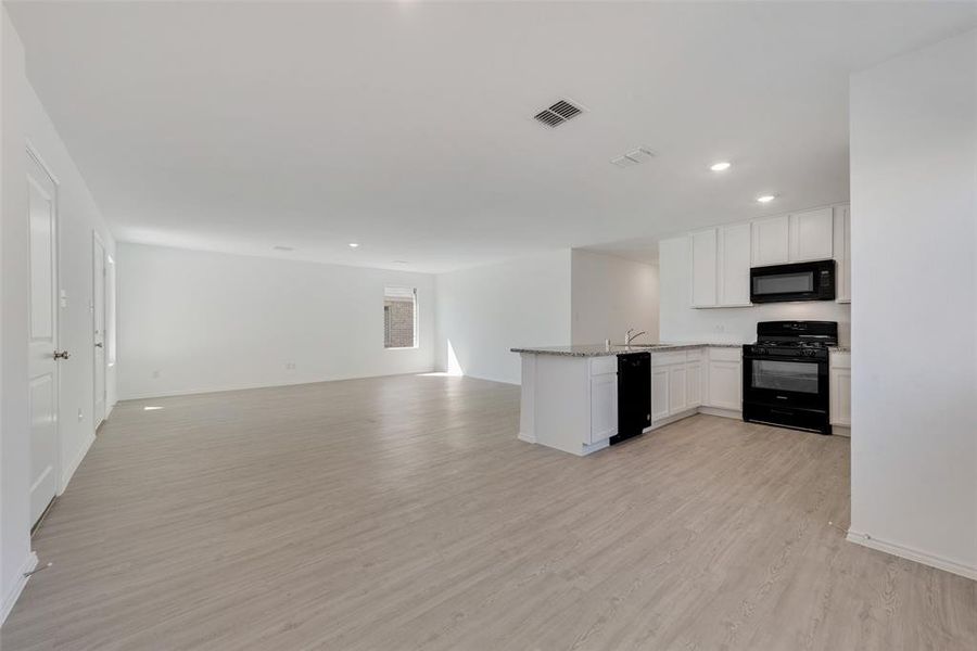 Kitchen with light wood-type flooring, sink, white cabinets, kitchen peninsula, and black appliances