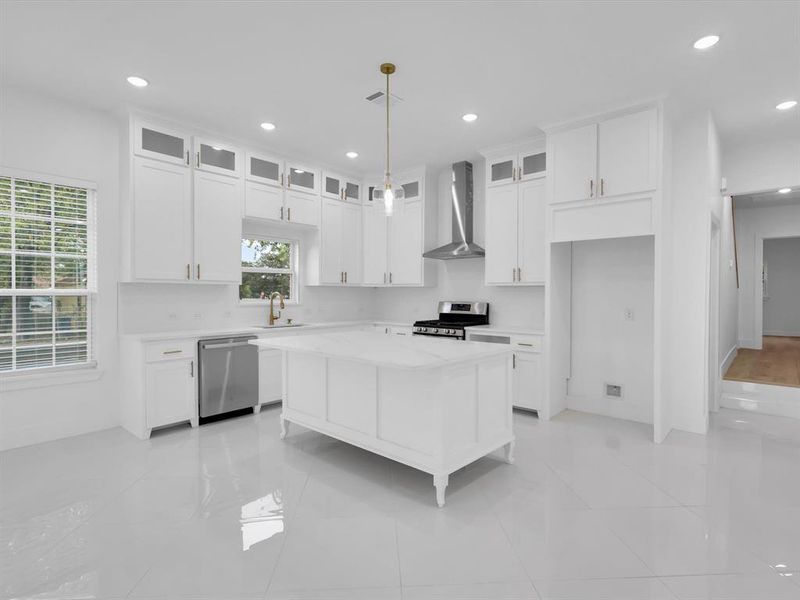 Kitchen with stainless steel appliances, a kitchen island, white cabinets, wall chimney range hood, and pendant lighting