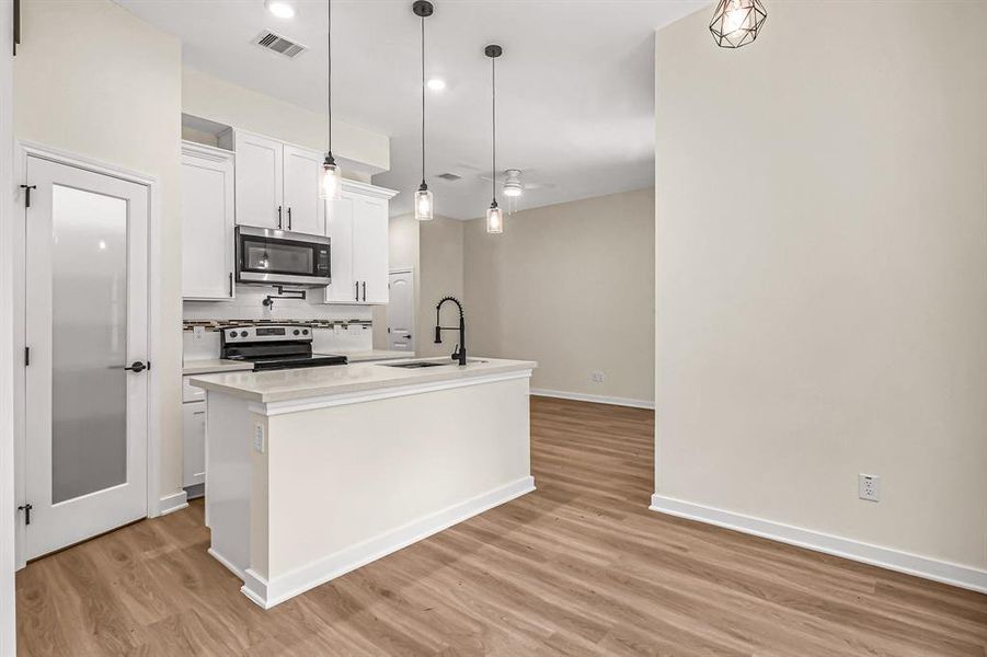 Kitchen is open to the living room beyond. Corner walk in pantry provides plenty of storage. Pot filler, designer tile backsplash and varied cabinet heights provide interest in this efficient kitchen.