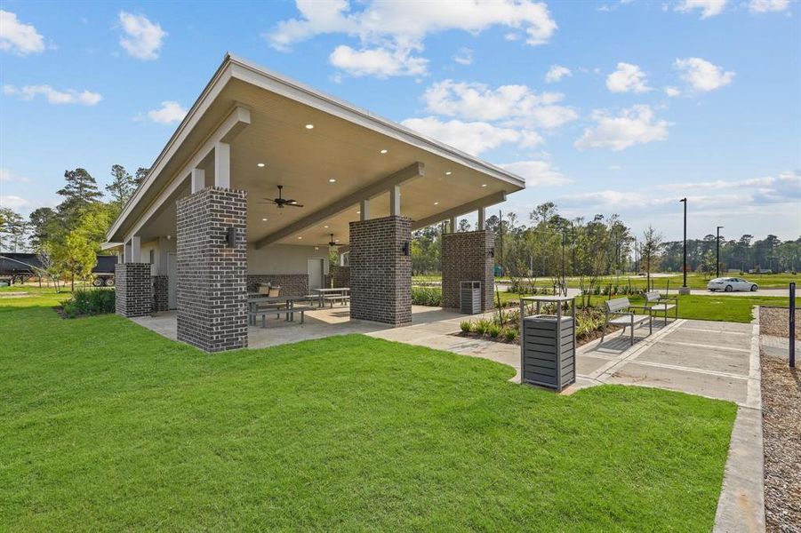 This modern outdoor pavilion has a spacious covered patio area, perfect for entertaining. It features high ceilings with fans, built-in seating, and a grill station, all set within a well-manicured lawn.