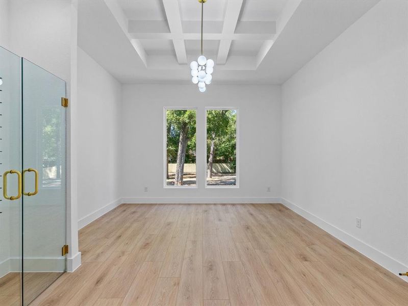 Spare room featuring an inviting chandelier, light wood-type flooring, beamed ceiling, and coffered ceiling