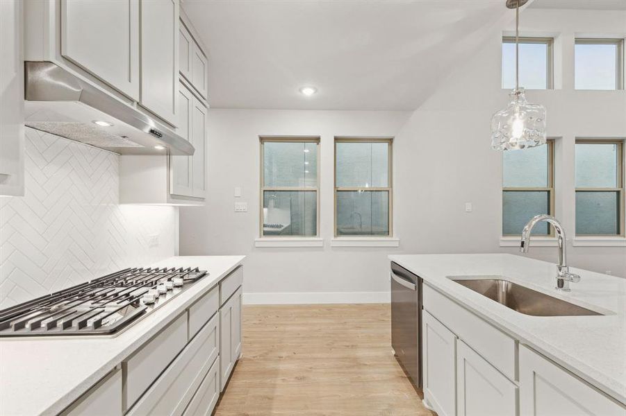 Kitchen with tasteful backsplash, hanging light fixtures, stainless steel appliances, sink, and light wood-type flooring