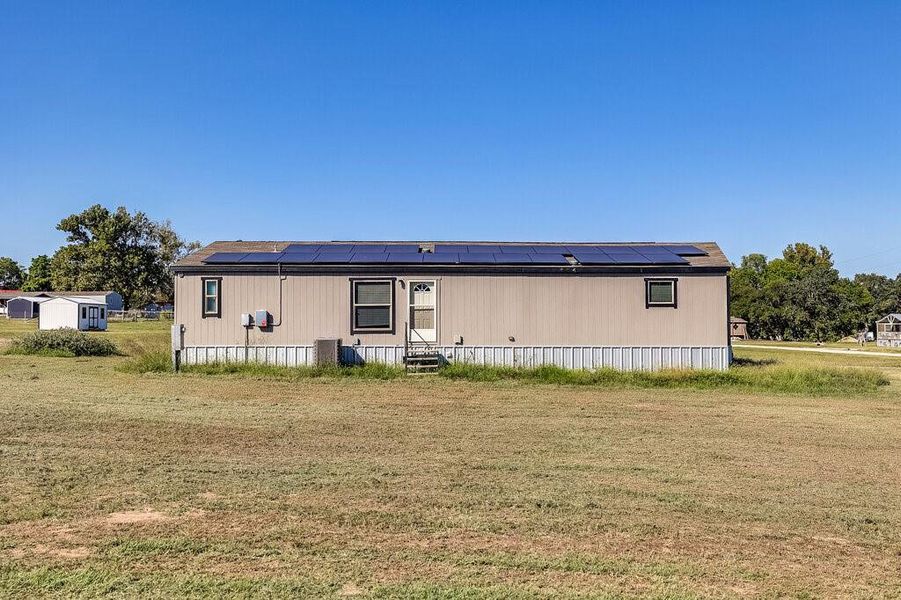 Back of house featuring a lawn and solar panels