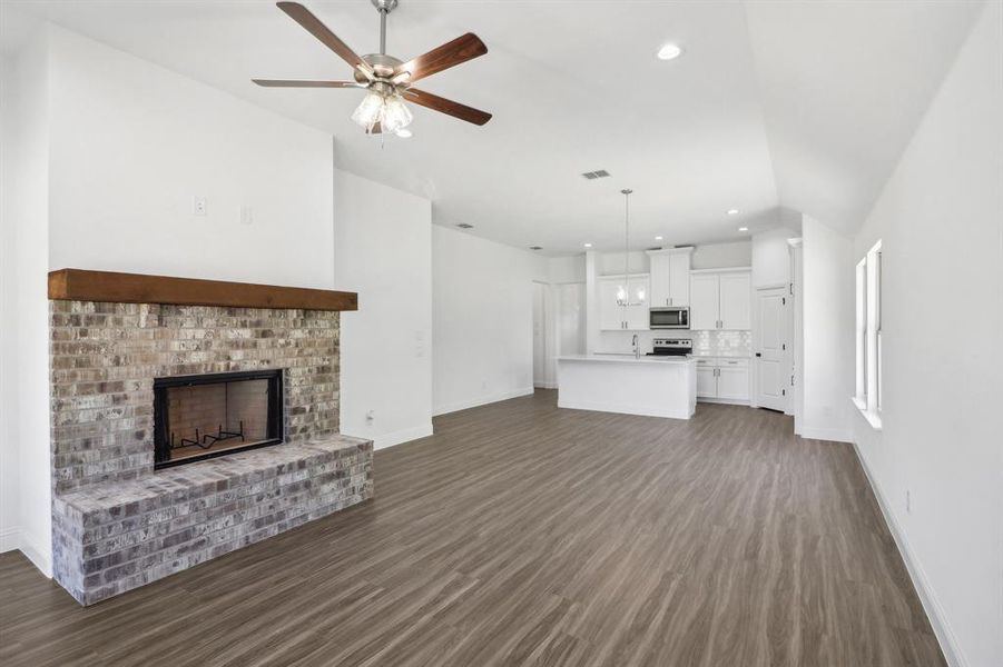 Unfurnished living room featuring ceiling fan, vaulted ceiling, a brick fireplace, and dark hardwood / wood-style flooring