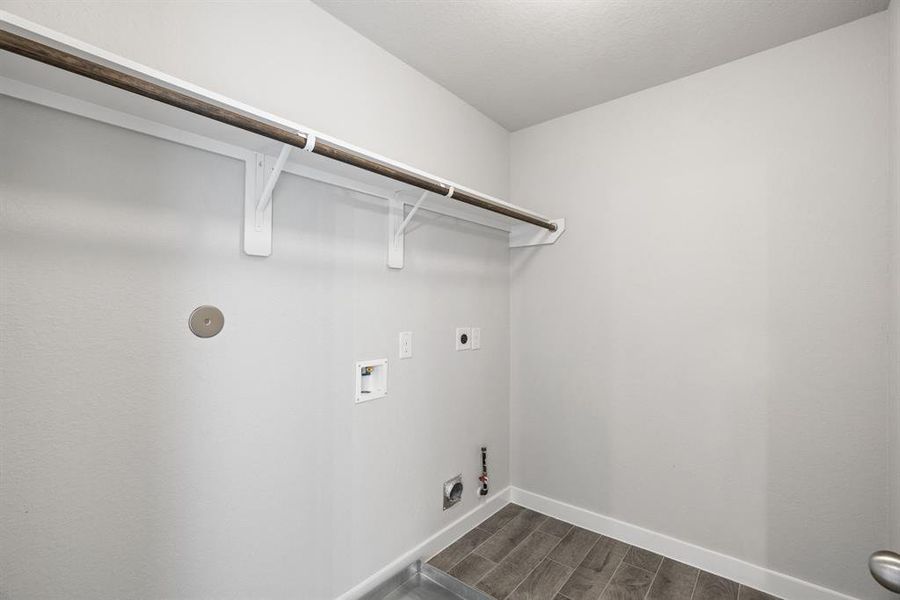 A spacious utility room with ample shelving for organization. It features connections for both gas and electric dryers, making it versatile and functional for all laundry needs. Sample photo, actual color and selections may vary.