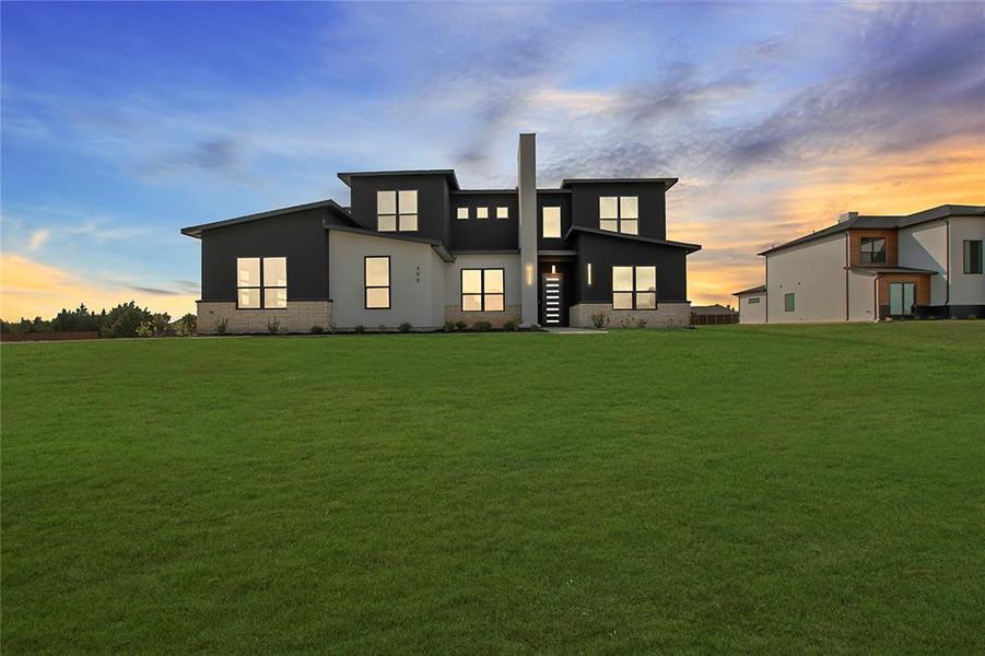 Back house at dusk featuring a lawn