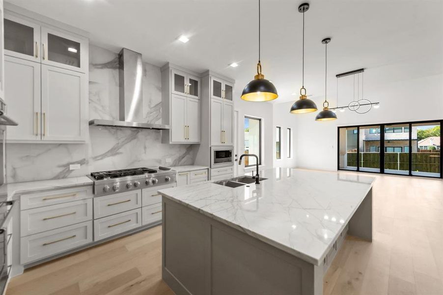 Kitchen featuring a kitchen island with sink, wall chimney exhaust hood, appliances with stainless steel finishes, and white cabinetry