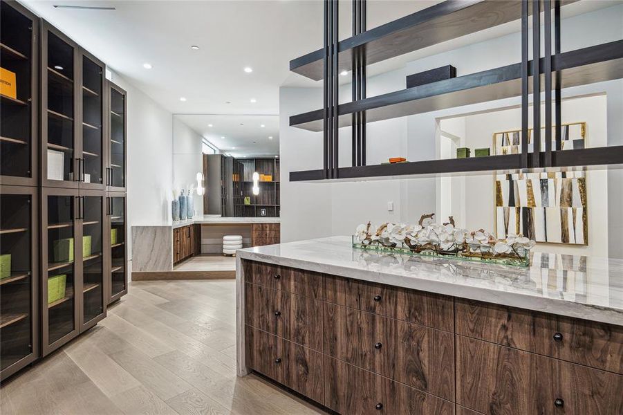 In the first of two primary closets, which is a meticulously designed space featuring dual levels for hanging and long hanging sections, providing ample storage for your wardrobe essentials. Transom windows allow natural light to filter in, creating a bright and airy atmosphere, while the elegance of stained White Oak Engineered Hardwood Flooring adds a touch of luxury to this functional and stylish retreat for organizing your attire.