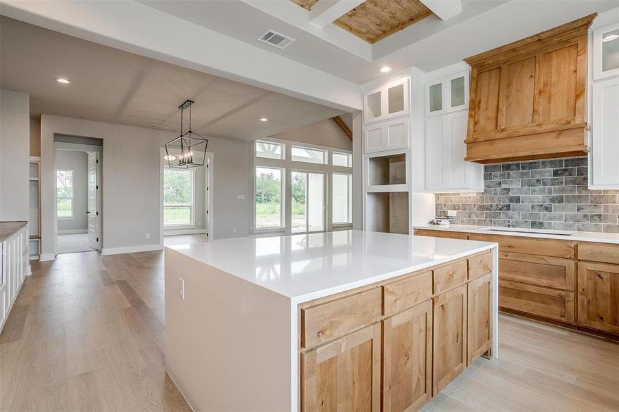 Kitchen featuring white cabinetry, light wood-type flooring, a kitchen island, pendant lighting, and tasteful backsplash