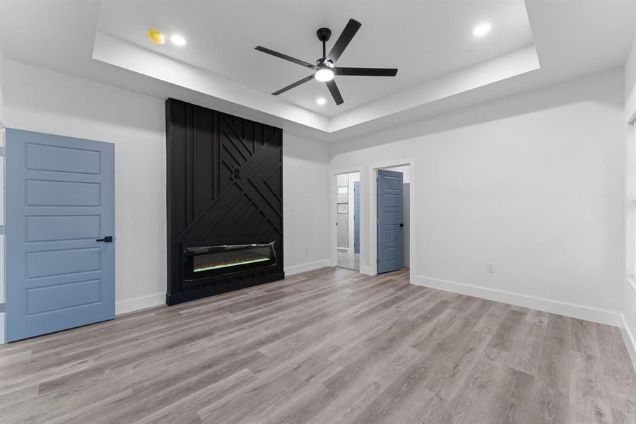 Unfurnished living room with ceiling fan, light wood-type flooring, and a raised ceiling