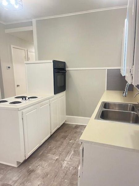 Kitchen featuring white cabinets, cooktop, light hardwood / wood-style floors, sink, and ornamental molding