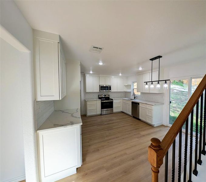 Kitchen with white cabinets, tasteful backsplash, decorative light fixtures, appliances with stainless steel finishes, and light wood-type flooring