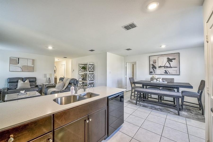 Kitchen featuring dishwasher, light tile patterned floors, dark brown cabinets, and sink