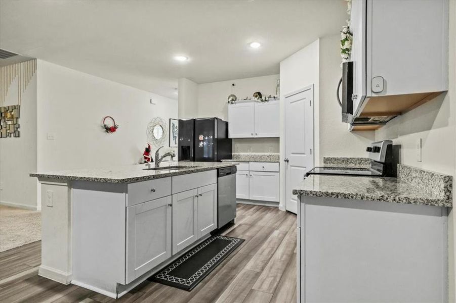 Kitchen featuring white cabinetry, wood-type flooring, stainless steel appliances, and a kitchen island with sink