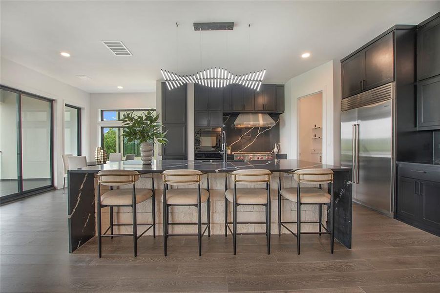 Kitchen featuring dark wood-type flooring, an island with sink, and stainless steel built in fridge