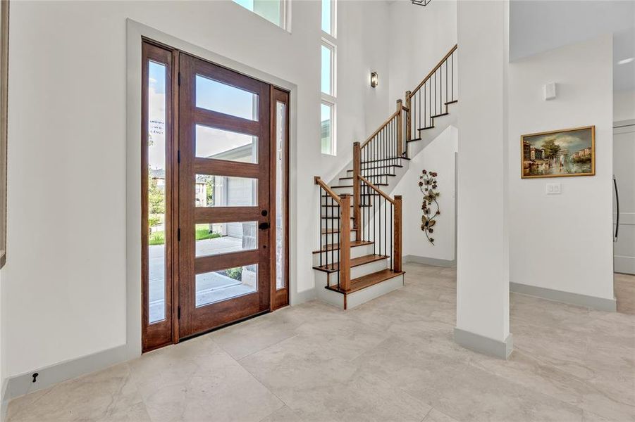 A bright entry way with a beautiful wooden front door, tile flooring and a staircase with metal balusters and wooden handrail.