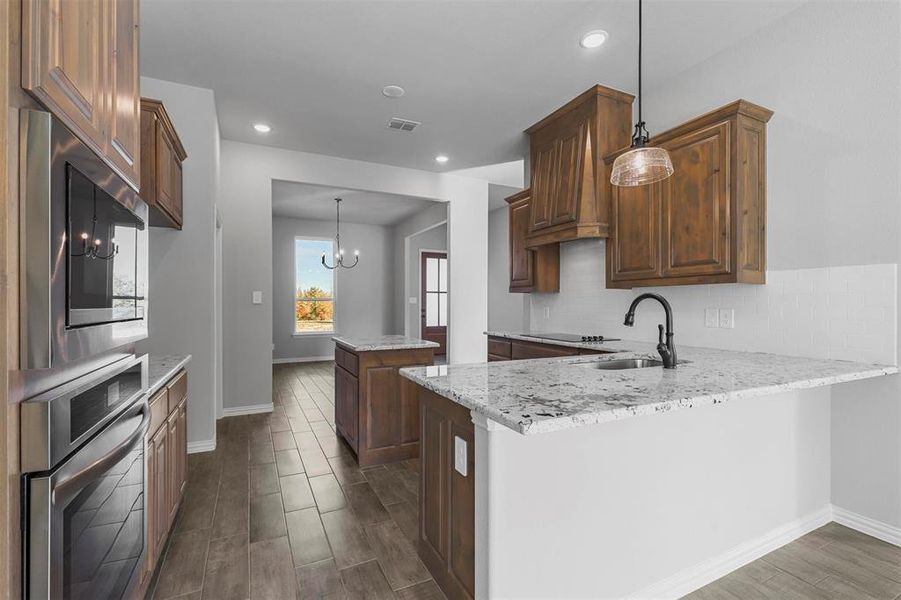 Kitchen featuring appliances with stainless steel finishes, a notable chandelier, sink, kitchen peninsula, and dark wood-type flooring