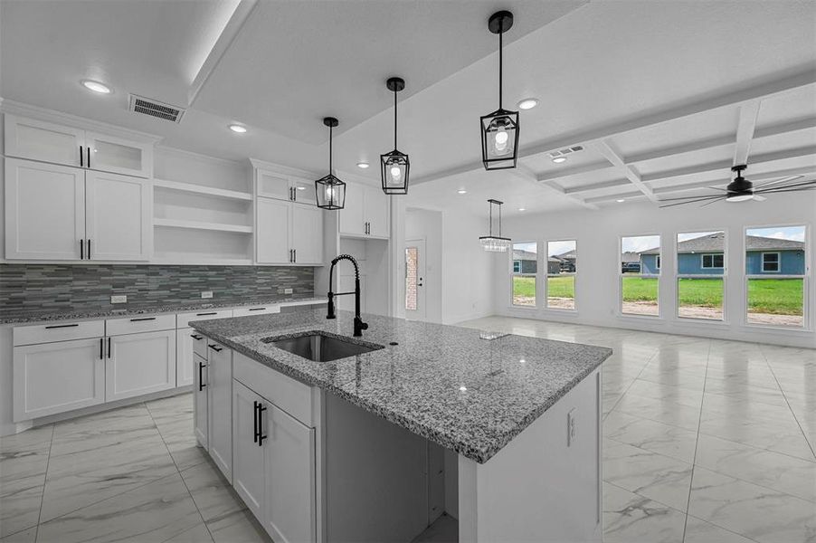 Kitchen with decorative light fixtures, light tile patterned flooring, white cabinets, sink, and backsplash