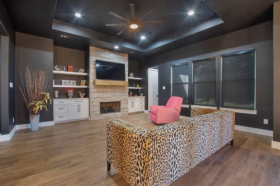 Living room featuring a stone fireplace, a tray ceiling, and dark hardwood / wood-style flooring