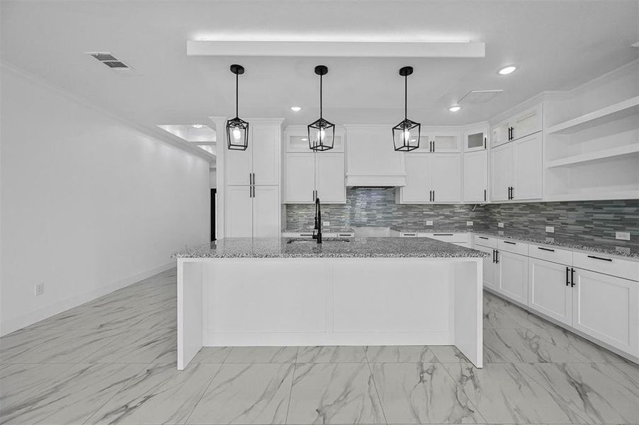 Kitchen featuring decorative light fixtures, white cabinetry, tasteful backsplash, light stone counters, and a center island with sink