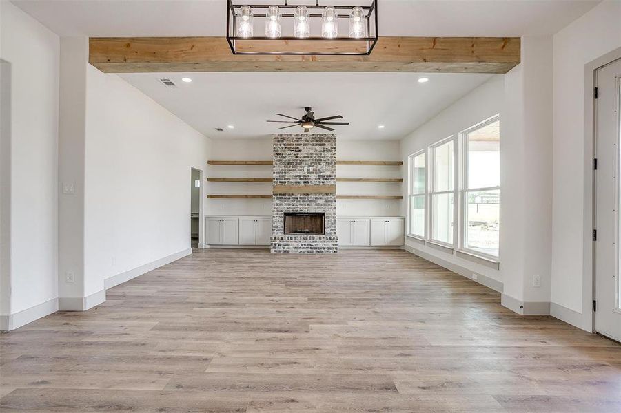 Unfurnished living room featuring ceiling fan, light wood-type flooring, beamed ceiling, and a brick fireplace