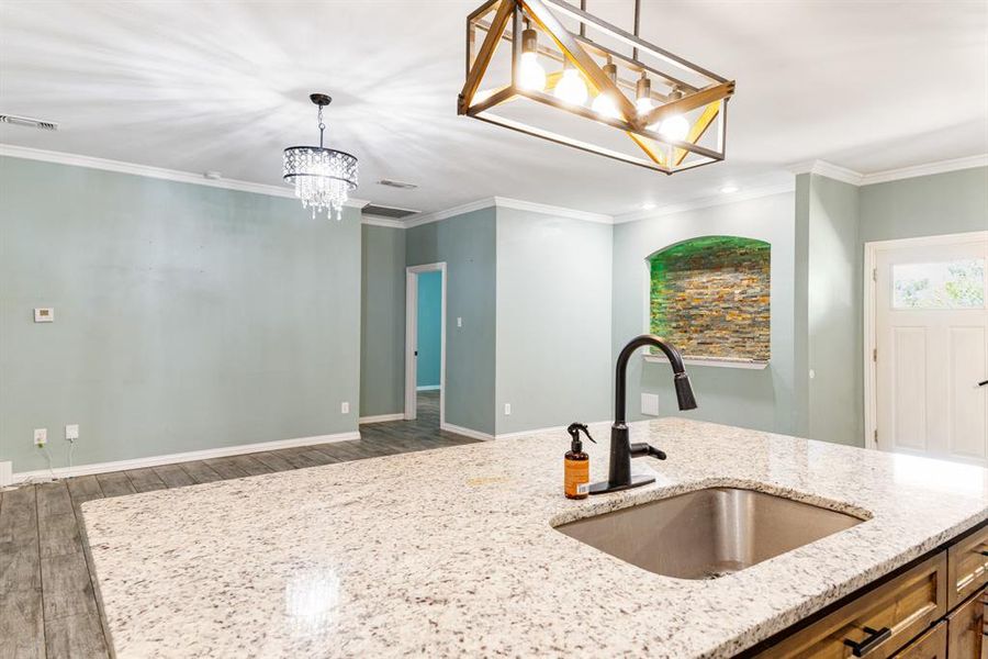 Kitchen featuring light stone counters, dark hardwood / wood-style flooring, pendant lighting, ornamental molding, and sink