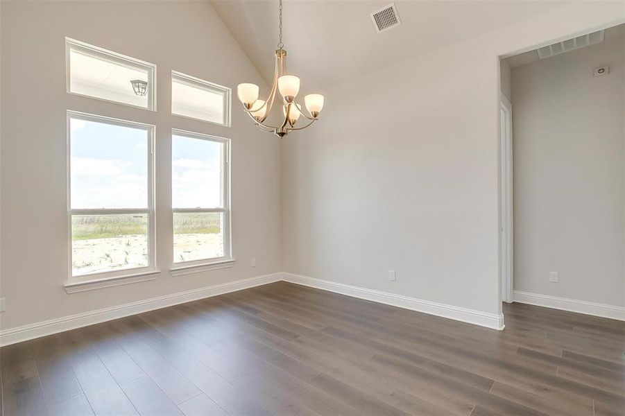 Spare room featuring dark wood-type flooring, high vaulted ceiling, and an inviting chandelier