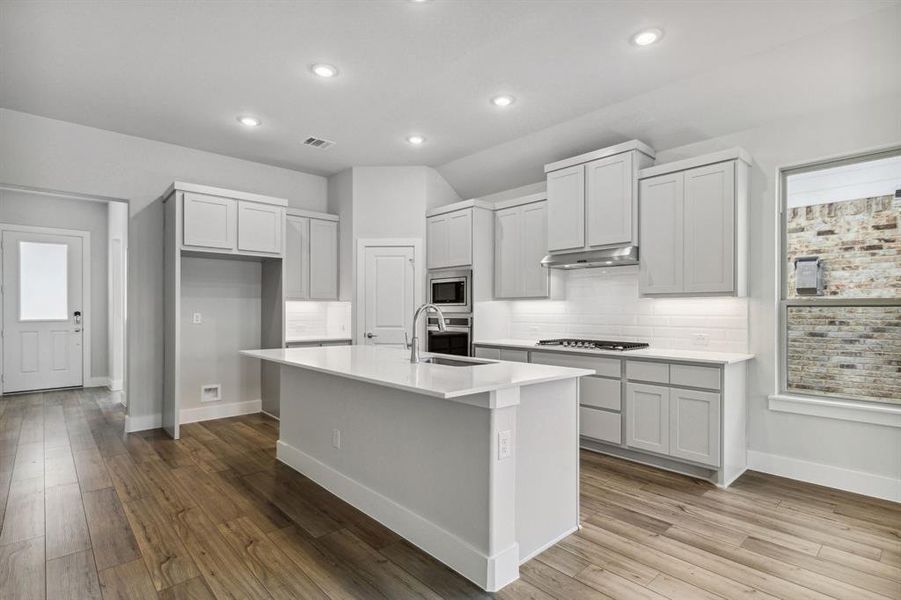 Kitchen featuring light hardwood / wood-style floors, a center island with sink, sink, appliances with stainless steel finishes, and backsplash