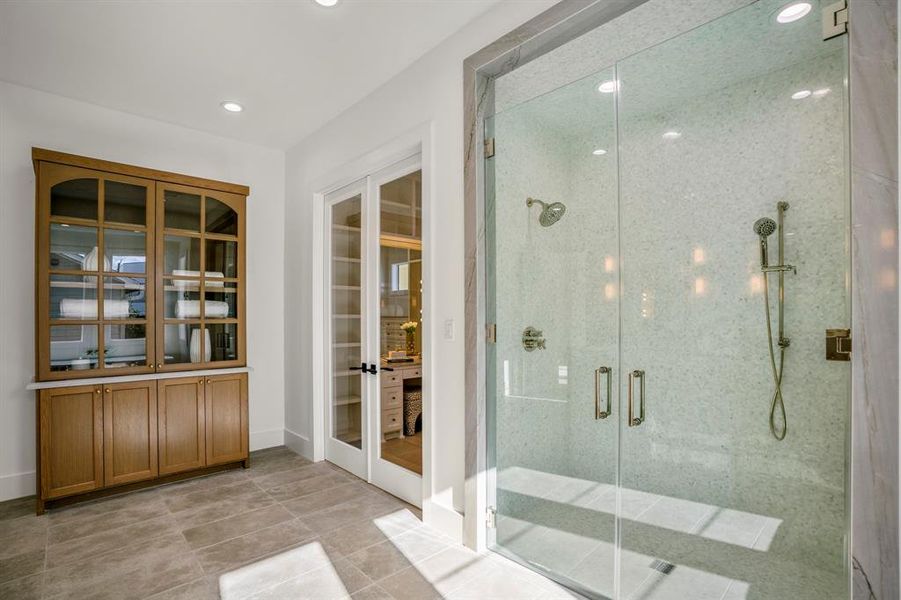 Double glass doors open up into your walk-in shower with a bench, hand held wand, and wall-mounted shower head. Custom linen closet built for this space.