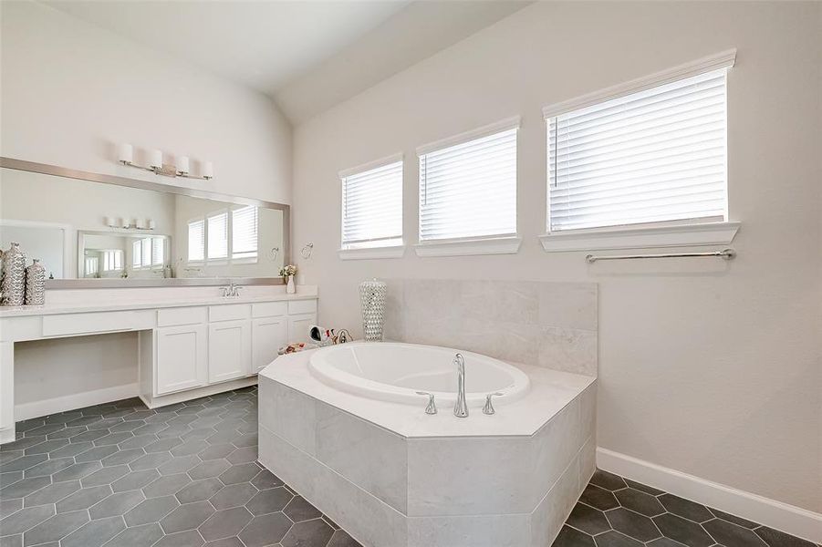 The primary bathroom has a vanity area and separate tub with tile surround.