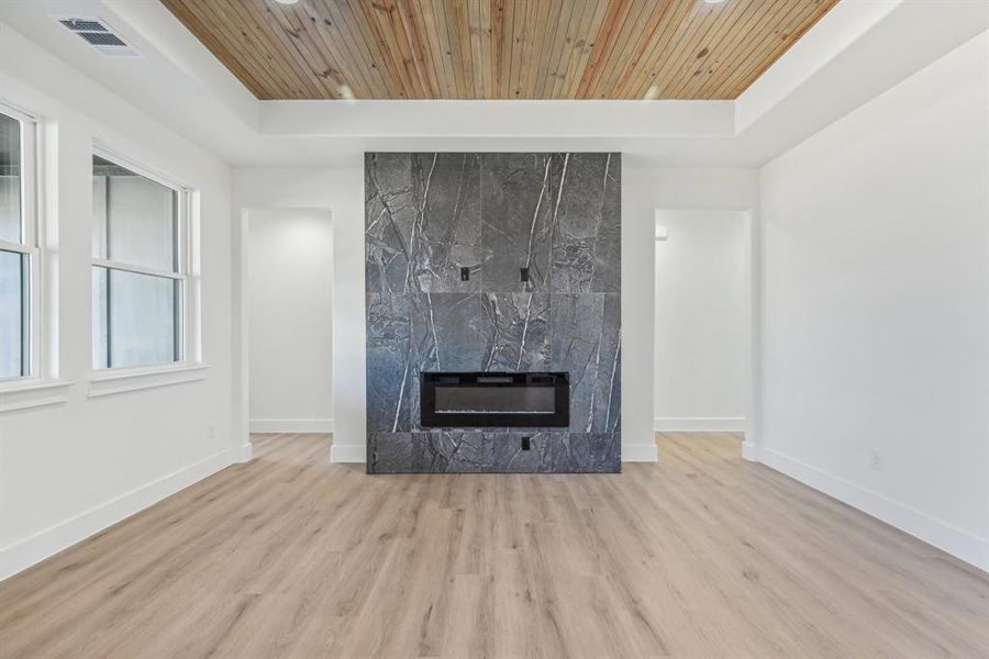 Unfurnished living room with a tray ceiling, light hardwood / wood-style flooring, a high end fireplace, and wooden ceiling