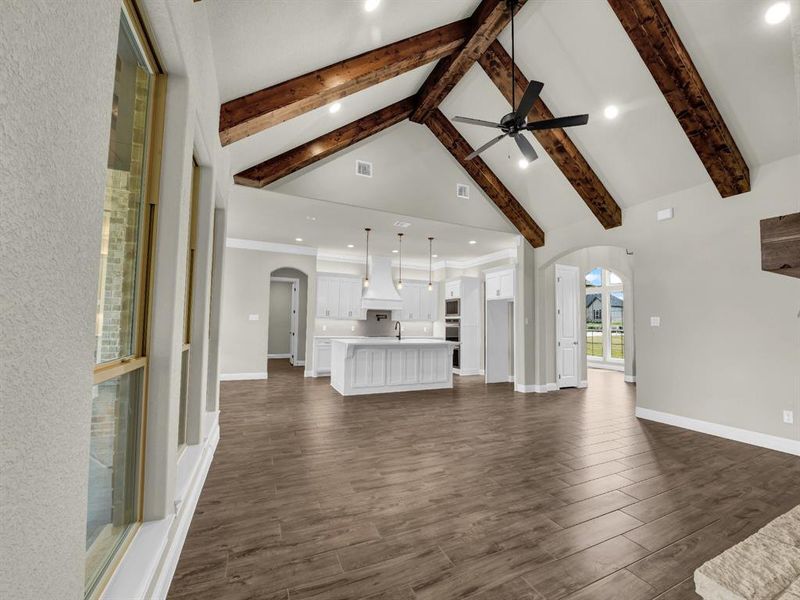 Unfurnished living room featuring dark wood-type flooring, ceiling fan, high vaulted ceiling, and beam ceiling