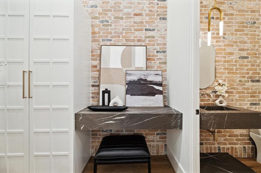The mudroom, with convenient access to the powder room, showcases a marble floating ledge, brick accent wall, and built-in cabinetry complete with shelving, combining practicality with aesthetic appeal.