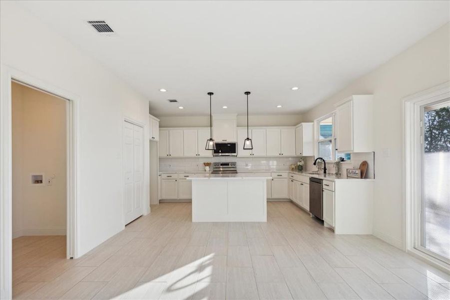 Kitchen featuring white cabinetry, a wealth of natural light, a kitchen island, and stainless steel appliances