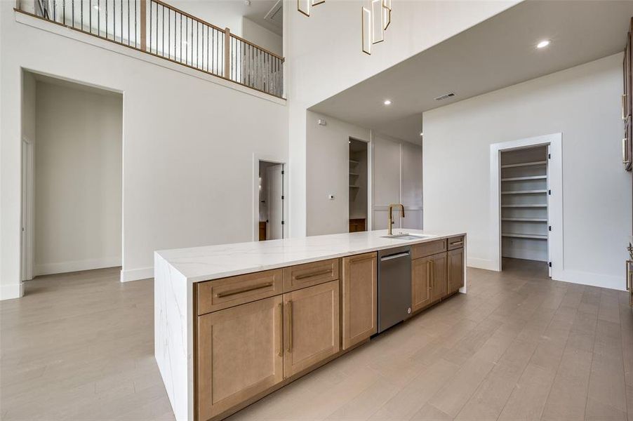 Kitchen with an island with sink, light wood-type flooring, dishwasher, a high ceiling, and sink